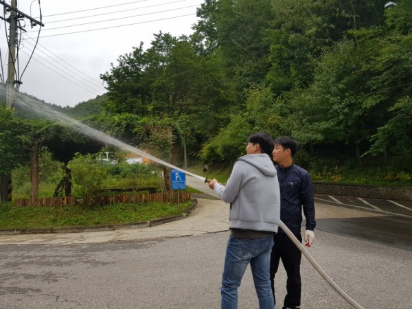 복지관의 젊은 남자 직원이 소방호스를 직접 사용해보는 훈련을 하고있다.